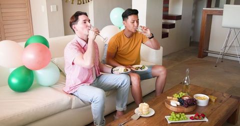 Gay Couple Celebrating at Home with Snacks and Drinks
