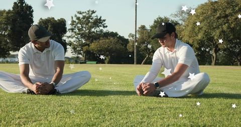 Cricket players stretching on green outfield wearing white polos and caps during warm-up