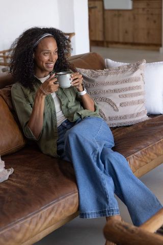 Cozy morning african american woman holding ceramic mug on leather sofa relaxed lifestyle