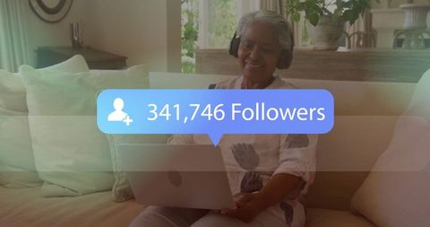 Elderly woman enjoying social media with headphones and laptop at home