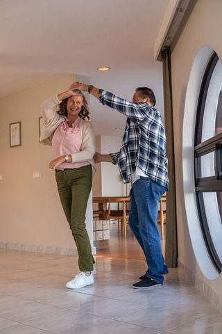 Joyful Mature Couple Dancing in Sunlit Hallway