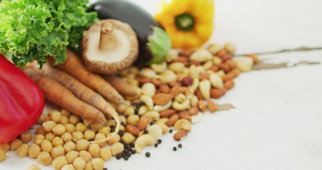 This image showcases a selection of fresh vegetables, nuts, and grains on a white table, including leafy greens, shiitake mushrooms, carrots, a red bell pepper, chickpeas, and a variety of mixed nuts. Ideal for illustrating content related to healthy eating on blogs, nutrition articles, vegetarian recipes, and organic lifestyle promotions. Can also be used for visual content in grocery advertisements or farm-to-table menus.