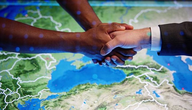 Shaking hands over digital map on touchscreen table representing global partnership