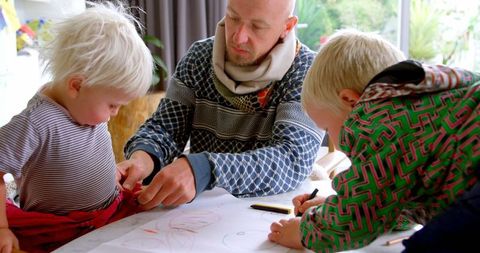 Father assisting child with drawing at family table