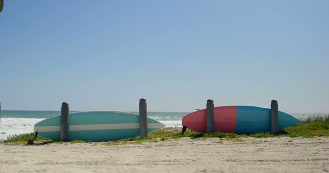 Two surfboards standing in the sand along the ocean, positioned vertically with stripes of blue and red colors. Ideal for themes related to beach vacations, surfing, water sports, and coastal landscapes. Useful for travel websites, summer promotions, surfing gear advertisements, and nature-oriented content.