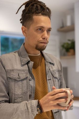 Man holding ceramic mug in modern kitchen, wearing denim jacket and quilted sweater, serene