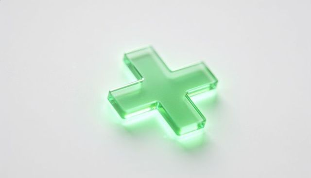 Glowing green acrylic plus symbol with beveled edges resting on white surface minimalist lighting