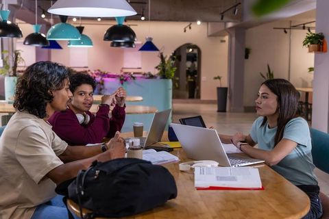 Young students collaborating on laptops in modern coworking cafe with study materials
