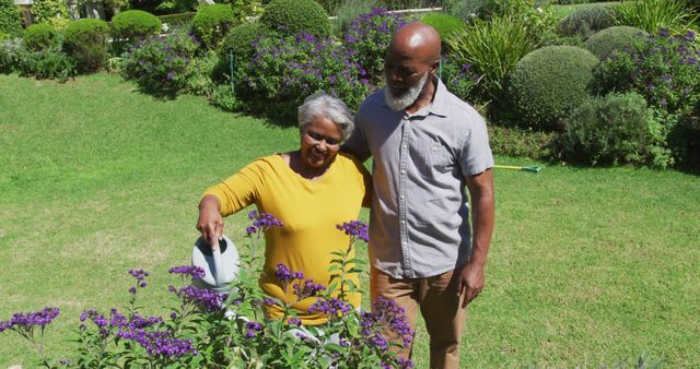 African american senior couple smiling while watering plants together in the garden. retirement senior couple lifestyle living concept