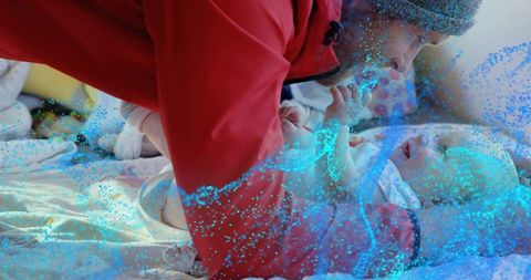 Father leaning over infant holding hands in cozy red jacket with blue particle overlay