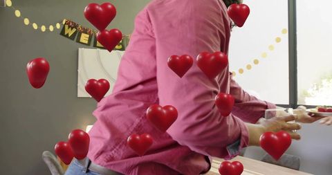 Man reaching for drink on table during home welcome party with floating red hearts