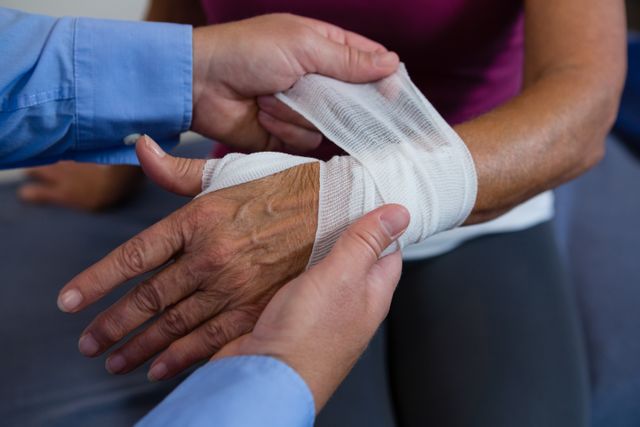 Physiotherapist putting bandage on injured hand of patient in clinic