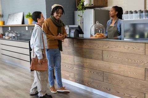 Diverse friends chatting at modern cafe counter with barista serving pastries and coffee