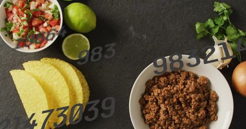 Flatlay seasoned ground beef with corn taco shells, pico de gallo, lime on rustic slate