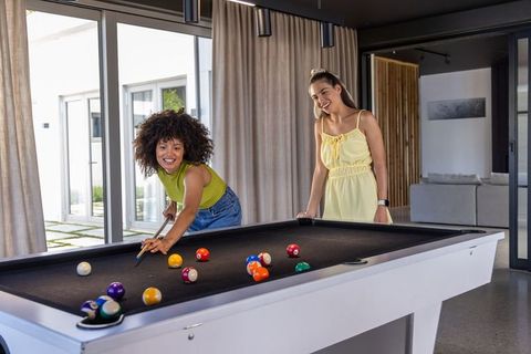 Diverse female friends playing pool in modern home lounge laughing and socializing