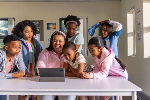 Teacher guiding tablet learning with diverse elementary students gathered around table