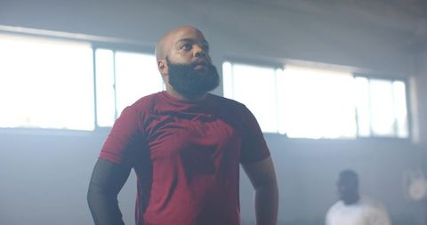 Backlit african american man training in gym wearing maroon tee and black compression sleeve