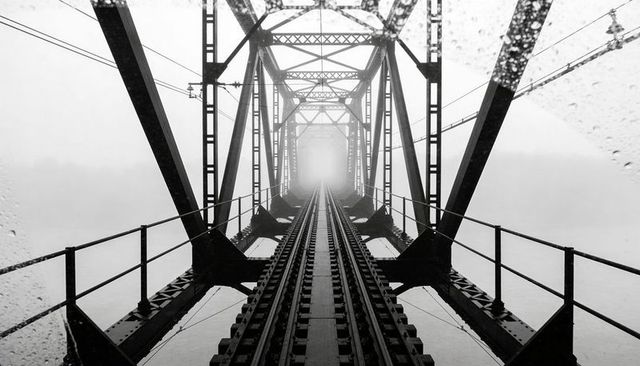 Centered steel railway tracks leading into fog on truss bridge with raindrops