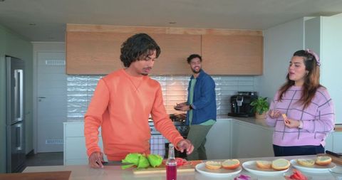 Young friends preparing burgers and chatting at modern kitchen island during casual gathering