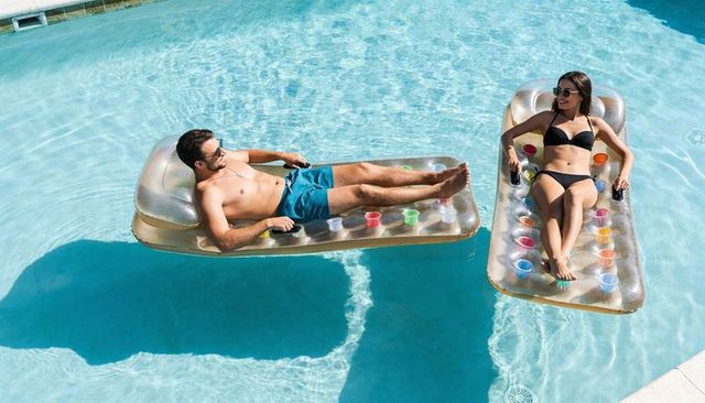Young couple relaxing on gold inflatable floats with colorful cup holders in backyard pool