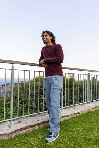 Asian man leaning on railing overlooking ocean at coastal viewpoint wearing maroon sweater