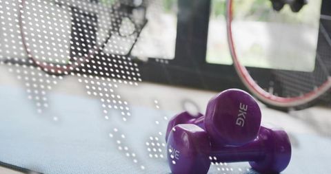Resting purple 3kg dumbbells on blue mat by sunlit window with bicycle wheel