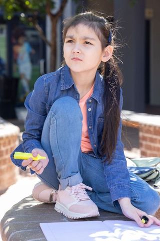 Pensive asian schoolgirl studying outdoors with yellow highlighter on urban bench