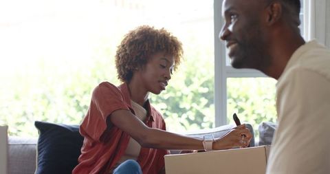 African American couple labeling moving boxes while unpacking in sunlit living room