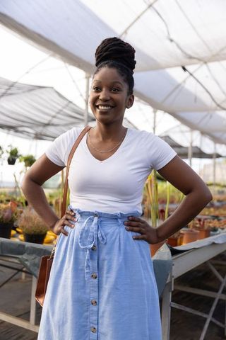 African american woman shopping in greenhouse nursery wearing white tee and blue skirt
