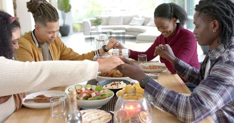 Multiracial friends holding hands around dinner table sharing meal and giving thanks