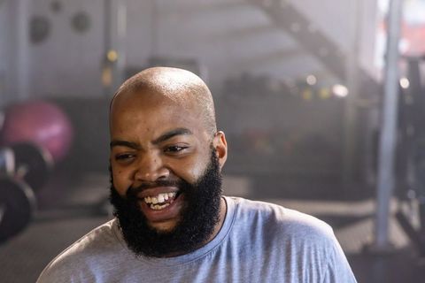 African american man laughing in gym wearing gray tee beard closeup with exercise ball