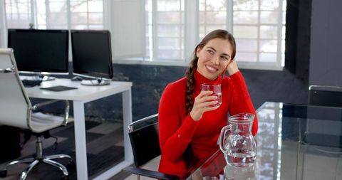 Businesswoman in Red Sweater Relaxing at Office Desk with Glass of Water