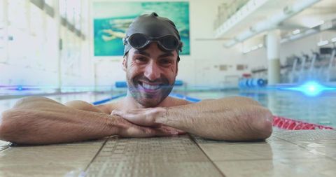 Smiling male swimmer resting at pool edge wearing cap and goggles after lap workout