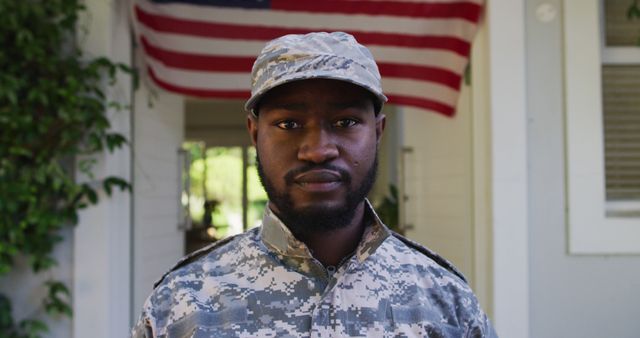 Portrait of african american male soldier standing in front of house and american flag. soldier returning home to family.
