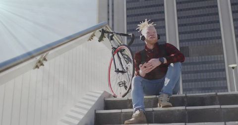 Man with Dreadlocks and Red Bike Enjoying Music on Urban Steps