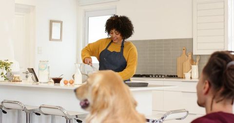 Woman whisking batter in sunlit modern kitchen while partner and dog watch