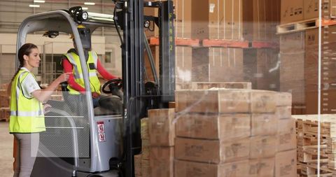 Woman directing forklift operator amid stacked pallets in warehouse logistics workflow