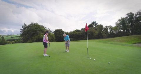 Senior couple putting on lush golf green with red flag and rolling countryside