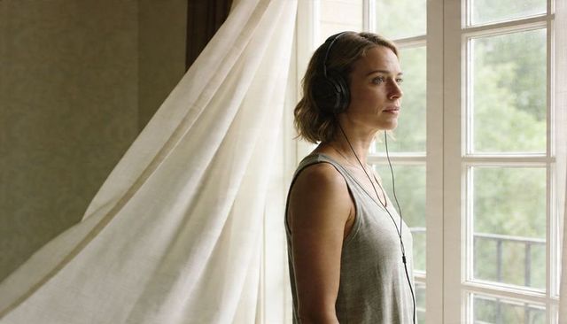 Woman listening to headphones at french doors gazing outside calm morning reflection