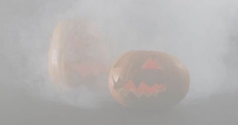 Glowing jack-o-lanterns in fog casting warm orange reflection on glossy moody surface