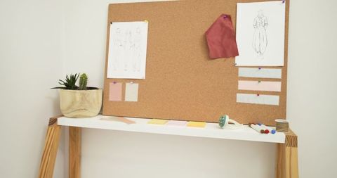 Corkboard moodboard with fashion sketches and burgundy fabric swatch above minimalist shelf