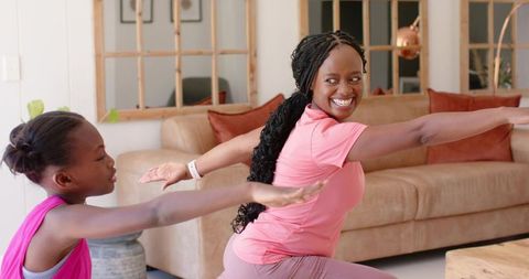 African mother and daughter practicing yoga at home together smiling during lunges