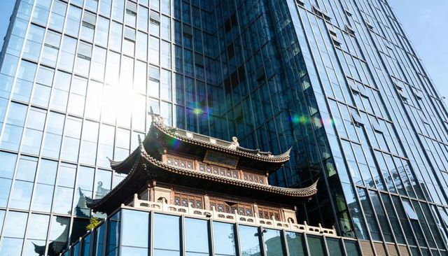 Traditional pagoda projecting from modern glass skyscraper with sun flare and reflections