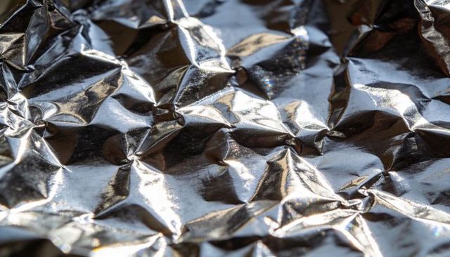 Crumpled aluminum foil reflecting light with iridescent shimmer macro metallic texture