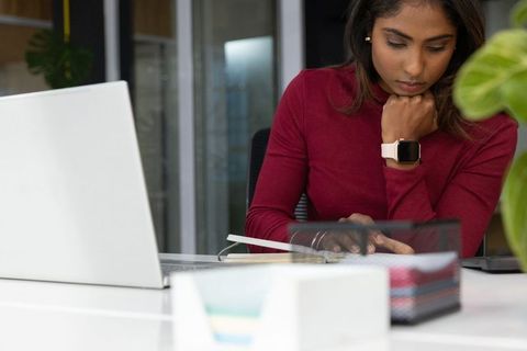 Indian woman working at desk reviewing planner with laptop and smartwatch boosting productivity