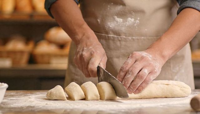 Baker Cutting Dough Into Portions on Floured Counter with Bench Scraper