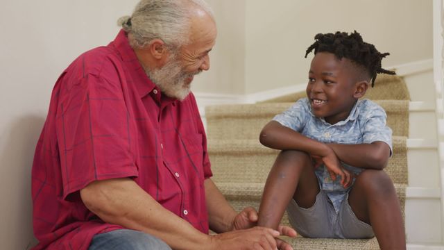 Senior African American man and his grandson spending time at home together, sitting on the stairs, the man tying the shoelaces on his grandson shoe, in slow motion.