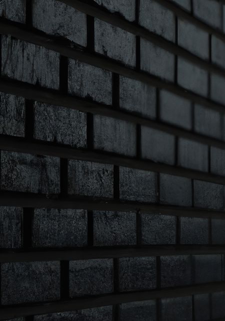 A full-frame close-up of a dark brick wall with a distinct horizontal line pattern. Ideal for use in architectural designs, construction themes, or as a grungy and textured background in graphic design projects.