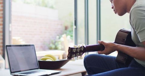 Man Practicing Guitar with Laptop in Sunlit Room