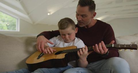 Father Teaching Son to Play Acoustic Guitar on Comfortable Sofa